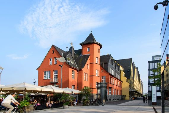 Das Rheinkontor im Rheinauhafen leuchtet in der Sonne, lebendiges Treiben in der Außengastronomie,